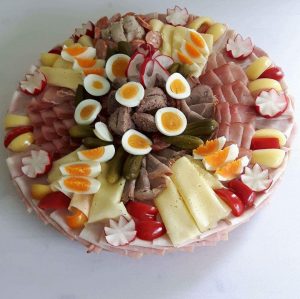 Kreisrunde Holzplatte belegt mit Aufgeschnittenem Käse, Wurde, Schinken dazu Eierspalten, Essiggurken und Rasieschenrosen